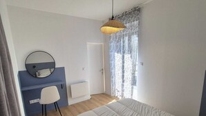 Un dormitorio con cama, escritorio, silla, lámpara colgante y ventana con cortinas.
