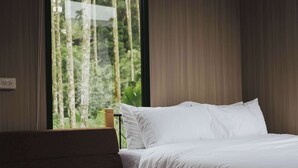 Un dormitorio con cama, un banco y ventana con vistas a árboles.