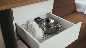 Un cajón de cocina con una olla de acero inoxidable, tazas blancas y una tetera blanca.