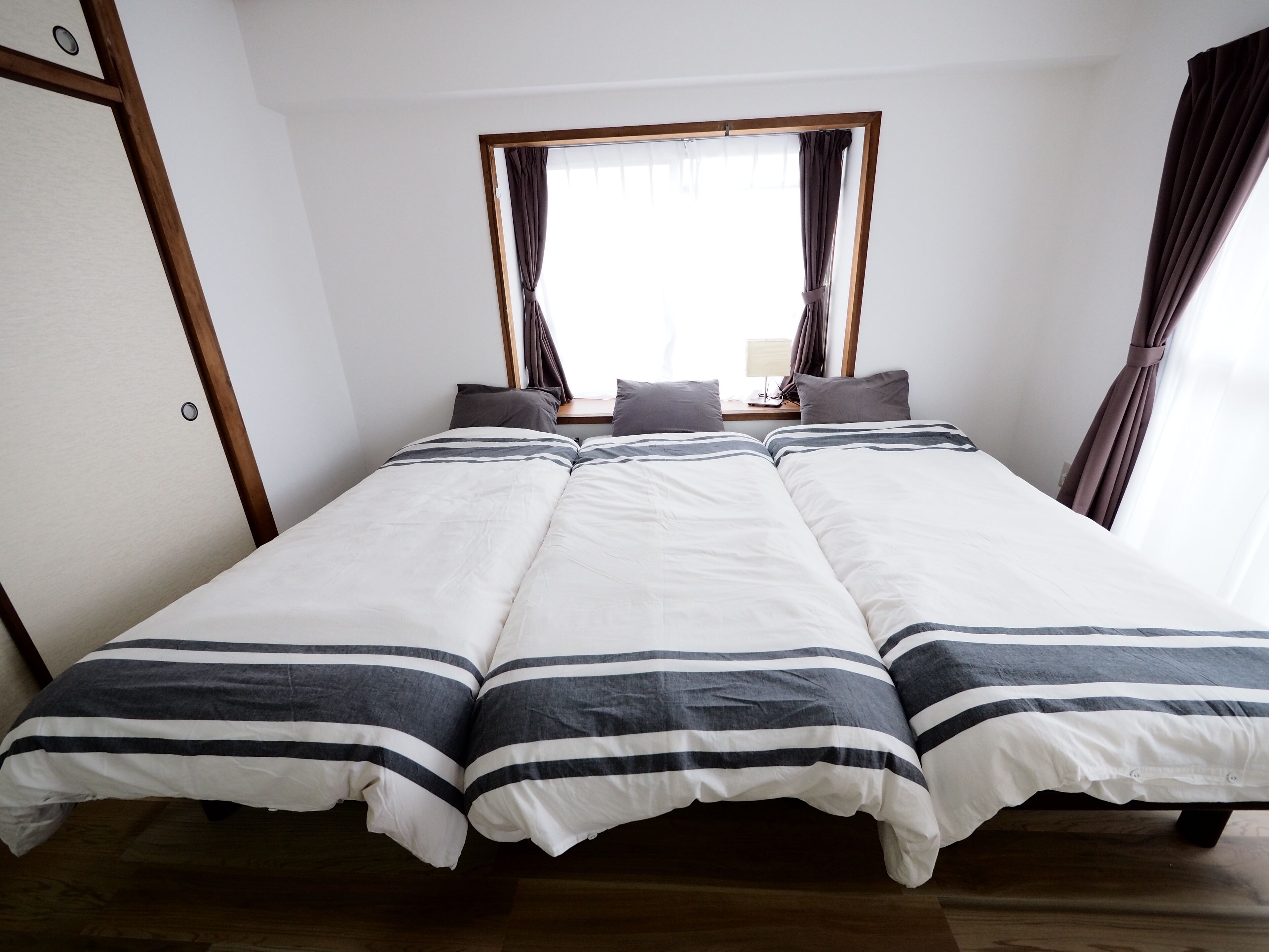 A double bed with striped bedding, a window with curtains, and a wooden floor.