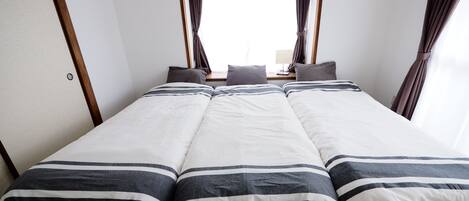 A double bed with striped bedding, a window with curtains, and a wooden floor.
