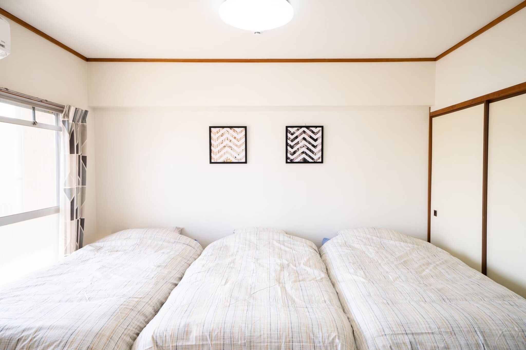 A room with a bed, a window with curtains, and two framed pictures on the wall.