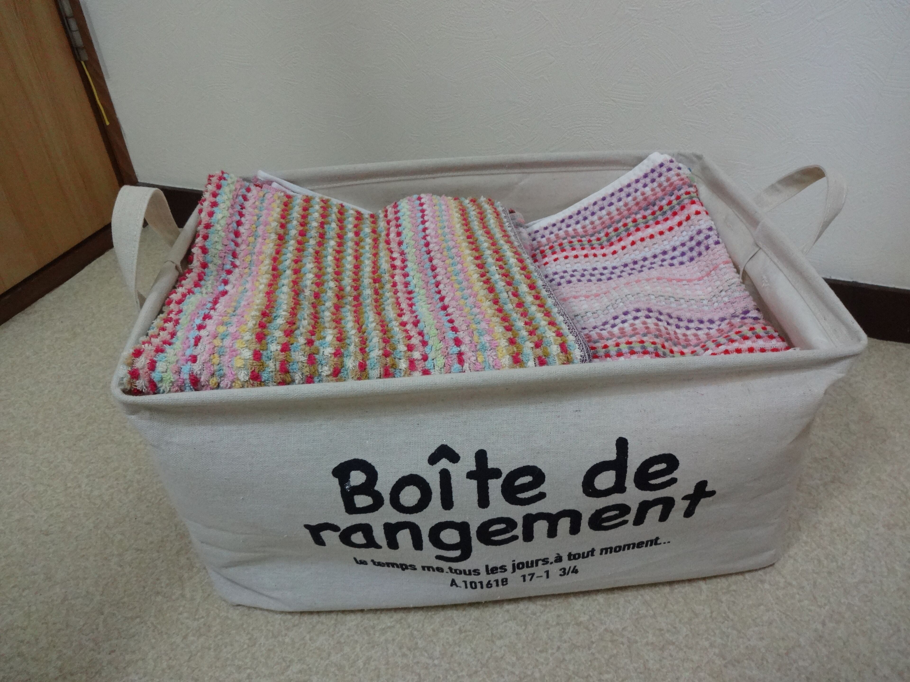 A storage bin labeled "Boîte de rangement" with colorful striped blankets inside.