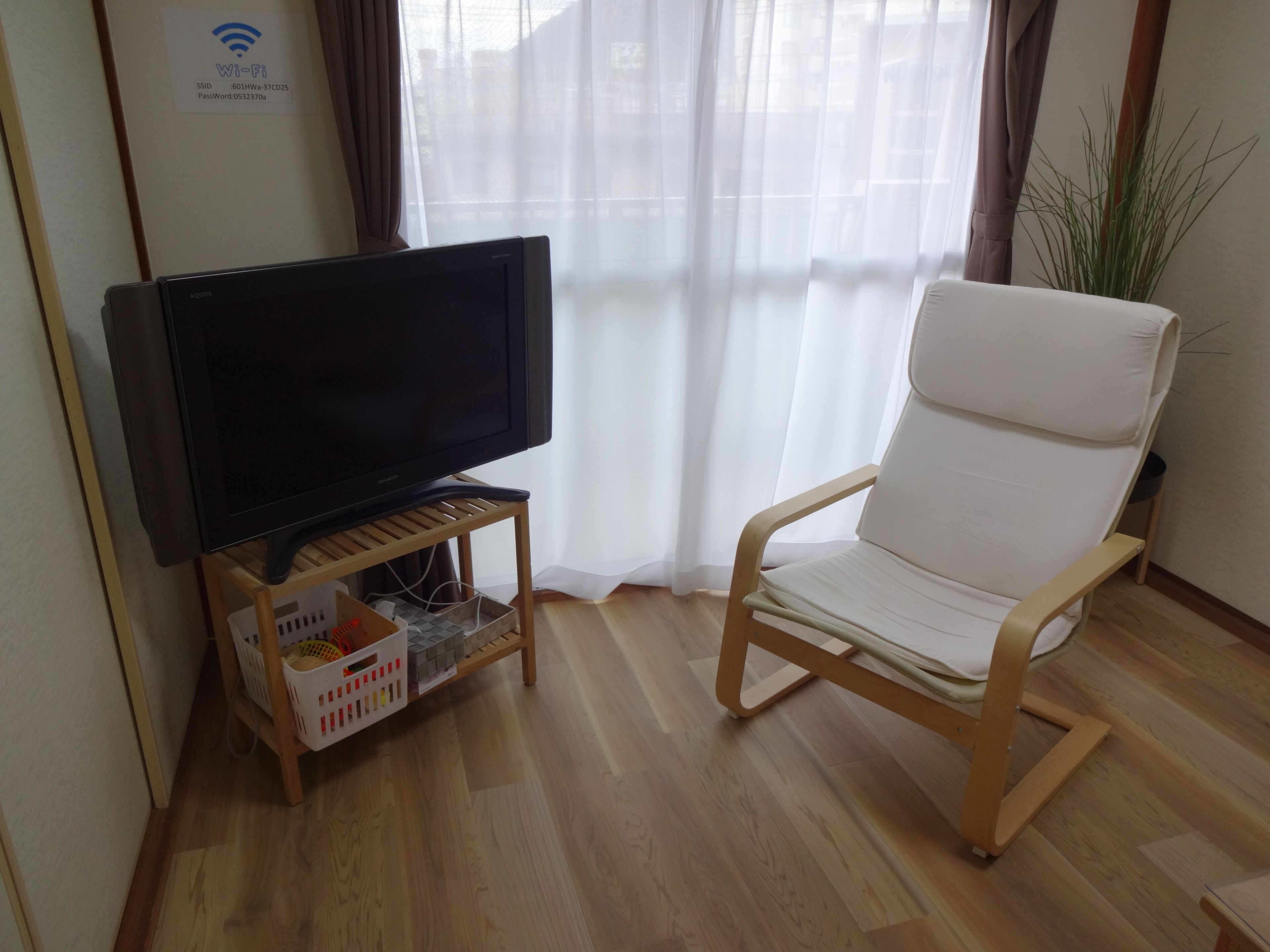 A living room with a flat-screen TV on a wooden stand, a white cushioned chair, and a potted plant.