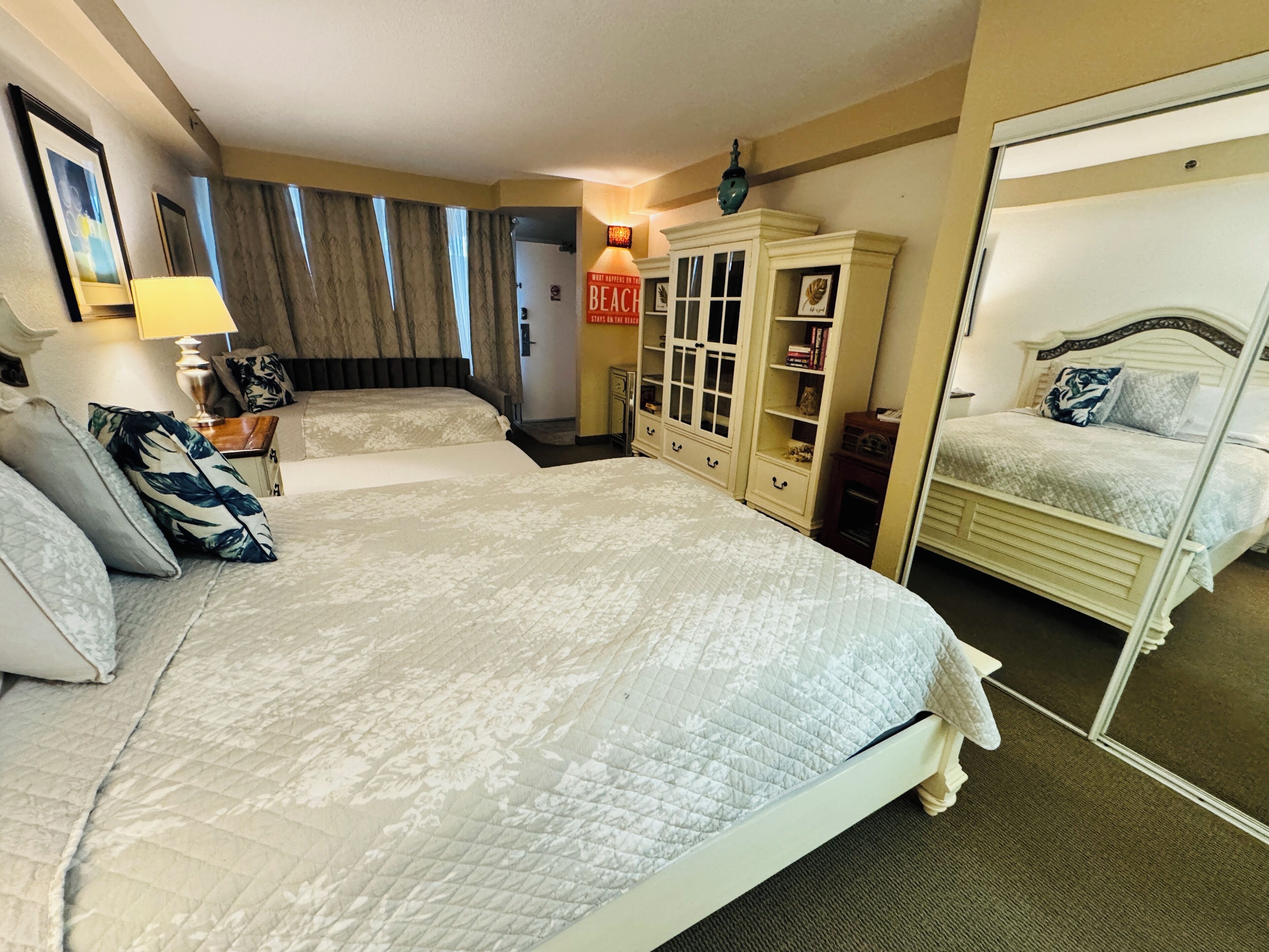 Une chambre d’hôtel avec deux lits, une armoire, un miroir et une lampe.