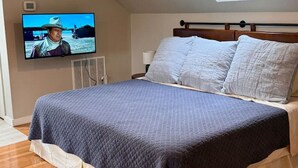Een slaapkamer met een bed, een televisie aan de muur, dakraam en een houten vloer.