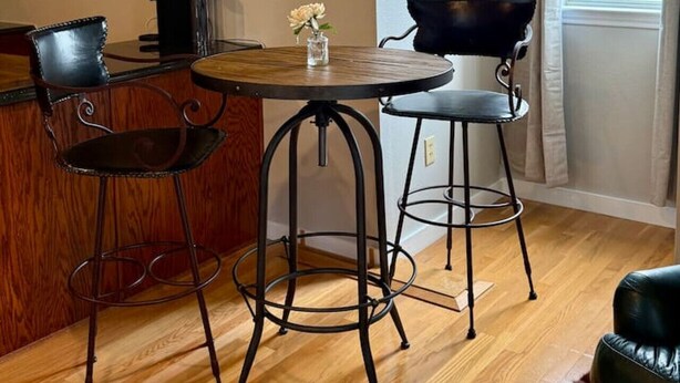Een eetruimte met een houten tafel en twee metalen stoelen, een kleine vaas met een bloem en een zwarte waterkoker op de tafel.