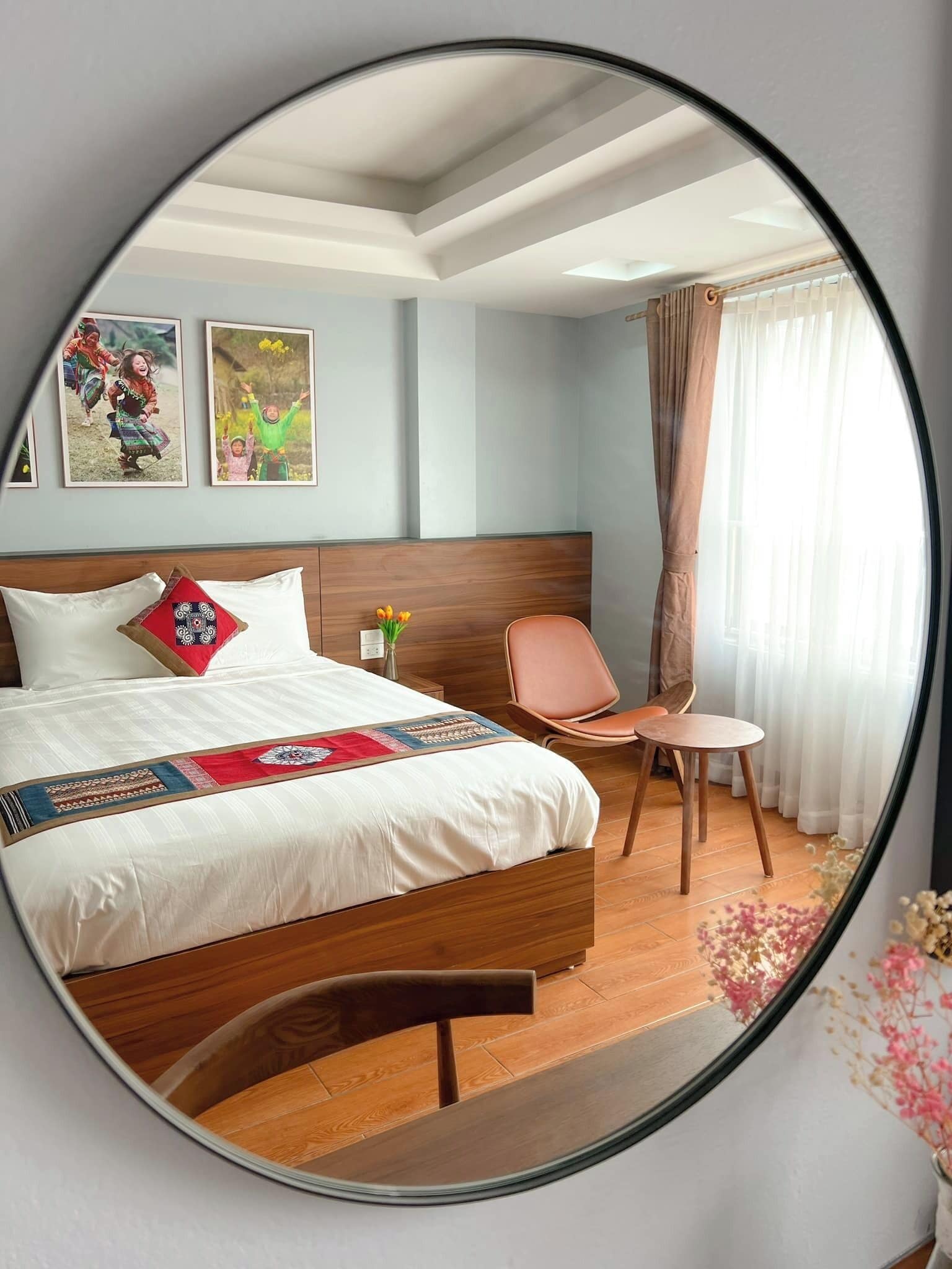 A bedroom with a large bed, a wooden headboard, a bedside table with a vase of flowers, and a chair.