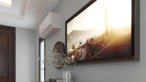 Un salon moderne avec un grand téléviseur à écran plat fixé au mur, une porte en bois foncé et un vase décoratif contenant des fleurs blanches, posé sur une table.