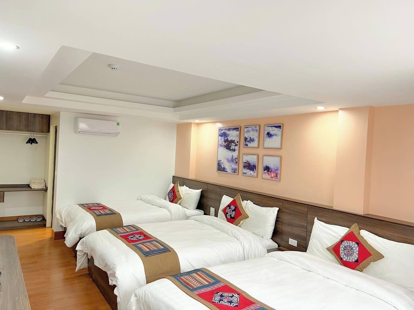 A hotel room with three beds, a wardrobe, an air conditioning unit, and artwork on the wall.