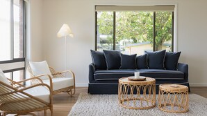 A modern living room with a dark blue sofa, two wicker chairs, a floor lamp, and a round coffee table. - Ocean View Escape, Gerroa (Gerroa)