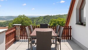 A patio with a table and chairs, a stone wall, and a view of a forested landscape.