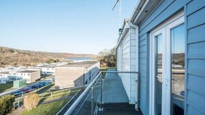A balcony with a metal railing overlooking a parking area and buildings. - Sea View Chalet | Walk to Freshwater Beach (Pembrokeshire)