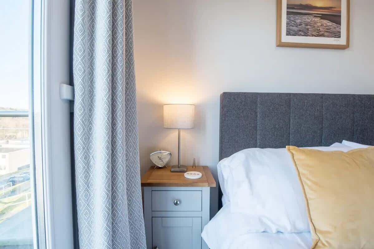 Habitació d'hotel amb un llit, una taula de nit amb una làmpada, un rellotge i un quadre al mur.