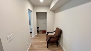 Un couloir avec un plancher en bois, une chaise et une porte au fond.