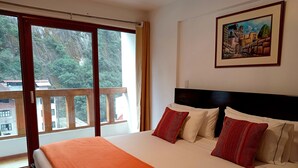Une chambre d’hôtel avec un grand lit, un tableau au mur et un balcon donnant sur des arbres et des immeubles.