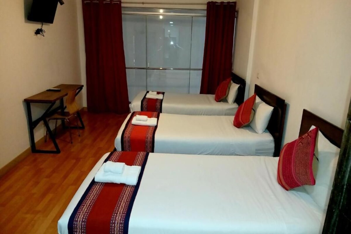 Habitación de hotel con dos camas, un escritorio, televisor y ventana con cortinas.