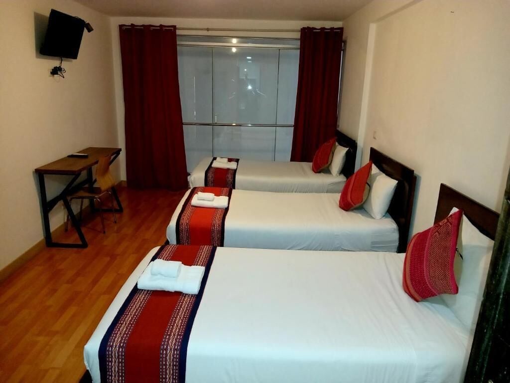 A hotel room with two beds, a desk, a TV, and a window with curtains.