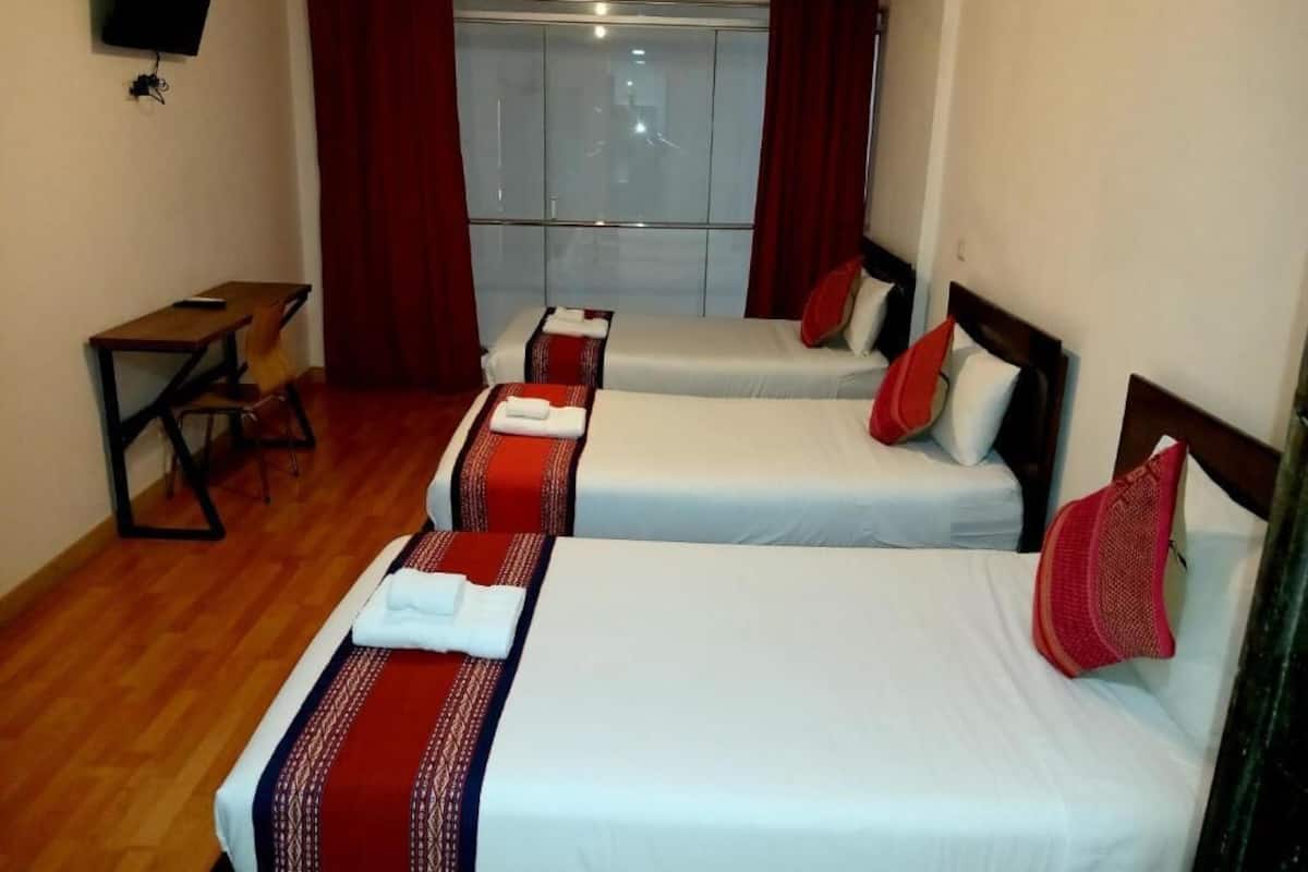 A hotel room with two beds, a desk, a TV, and a window with curtains.