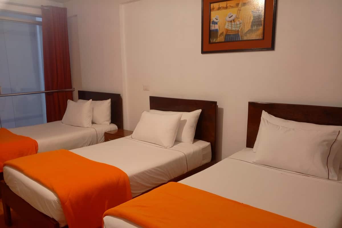 A hotel room with three beds, each with white bedding and orange throw blankets. There is a painting on the wall above the beds.