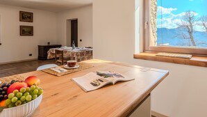 A dining area with a wooden table, a bowl of fruit, and a window with a mountain view.