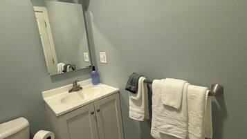 Un baño con inodoro, lavamanos, espejo, toallero y una alfombra oscura.