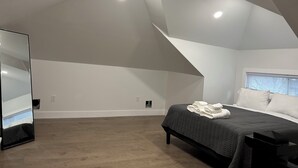 A bedroom with a sloped ceiling, a bed with a dark quilt, a bedside table, and a window with blinds. - Newly remodeled Spacious 4-BM house in Phoenixville with OS parking/ central, AC (Phoenixville)
