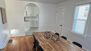 A spacious dining area with a long wooden table and black chairs, white cabinets, and a window with blinds. - Newly remodeled Spacious 4-BM house in Phoenixville with OS parking/ central, AC (Phoenixville)