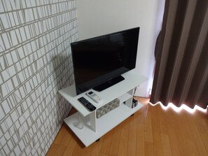 Un téléviseur à écran plat posé sur un meuble blanc, accompagné d’une télécommande et d’une multiprise.