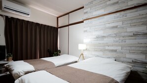 Camera d'albergo con due letti, una TV a schermo piatto, condizionatore d'aria a parete e una parete moderna con motivo in mattoni.