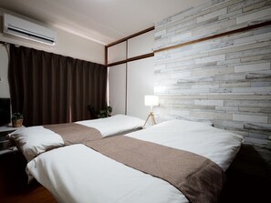 A hotel room with two beds, a flat-screen TV, a wall-mounted air conditioner, and a modern brick-patterned wall. - Living CUBE Beppu Station (Beppu)