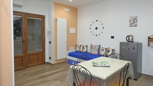 A compact living space with a bed, a dining table, a refrigerator, and a wall clock.