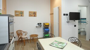 A compact living space with a kitchenette, a dining area with a table and chairs, a television mounted on the wall, and a bathroom visible through an open door.