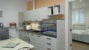 A compact kitchen with white cabinets, a stove, and a microwave. There is a dining table with chairs and a small refrigerator.