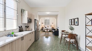 Eine moderne Küche mit großem Fenster, ein Essbereich mit Tisch und Stühlen sowie ein Wohnzimmer mit Sofa und Couchtisch.