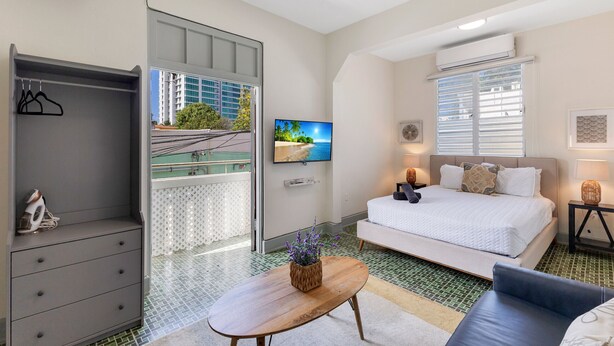 Ein modernes Hotelzimmer mit Bett, Fernseher, Schreibtisch und Blick auf eine Stadtlandschaft durch ein großes Fenster.