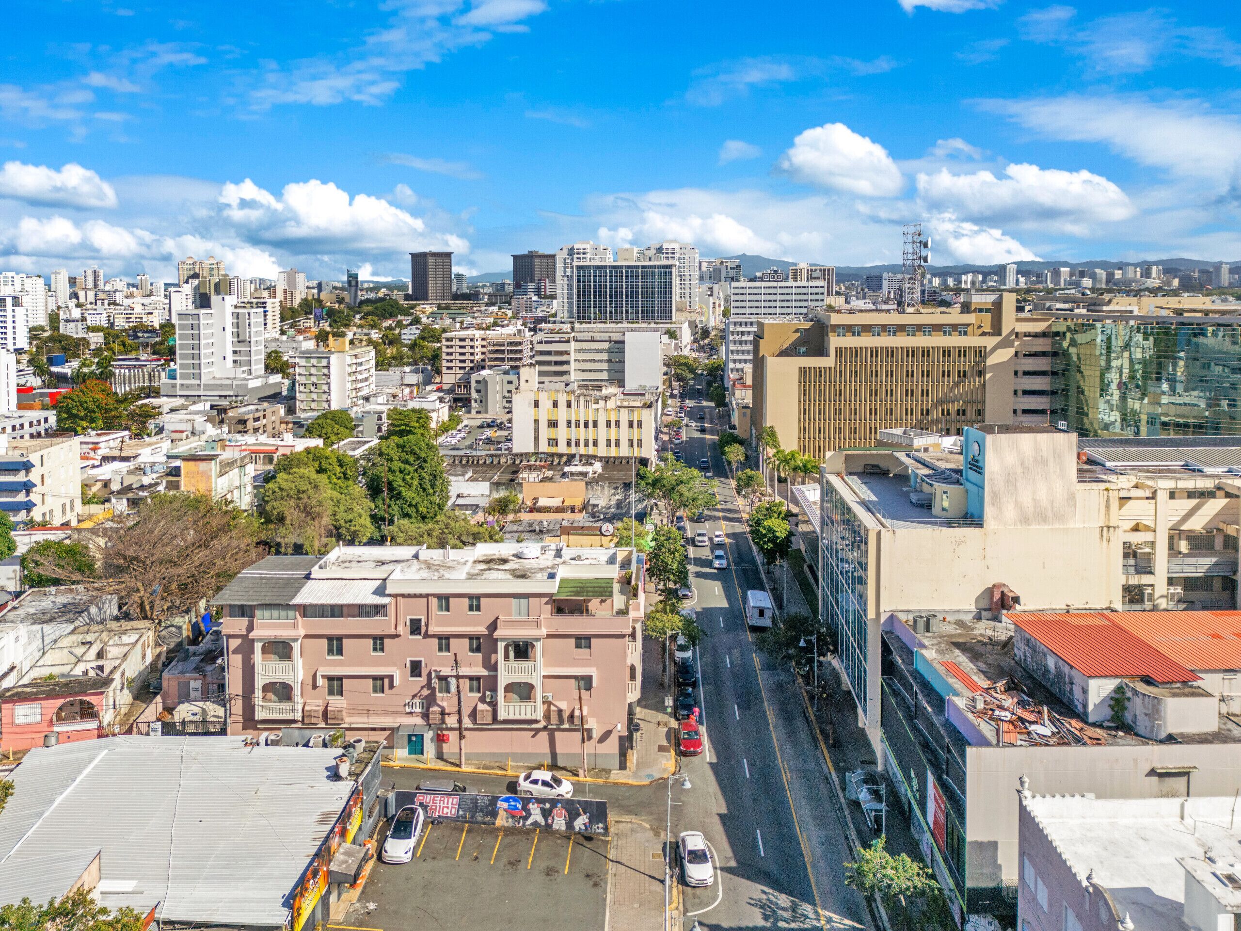 Un paysage urbain mêlant bâtiments modernes et bâtiments plus anciens, un ciel dégagé et une zone de stationnement avec des voitures.