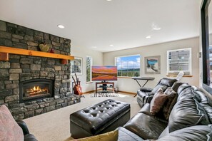 A living room with a stone fireplace, a leather sofa, a television, and artwork on the walls. - Beautiful Views, Game Room, EV Charger, Weber BBQ (Truckee)