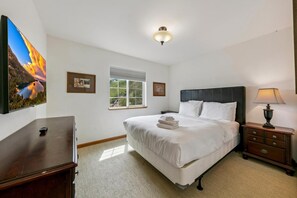 A bedroom with a bed, bedside table, lamp, window, and artwork on the wall.