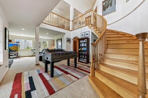 A spacious living area with a foosball table, a bookshelf, and a staircase.