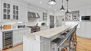 A modern kitchen with white cabinetry, a central island, and a built-in oven. - Luxury Home. Blue Valley Views. Extraordinary Attention to Detail | Sevenoaks Cottage (Highlands)