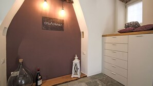 Een kamer met een stenen vloer, een houten plank met een fles en een lantaarn, een wit kastje met lades, en een bord aan de muur.