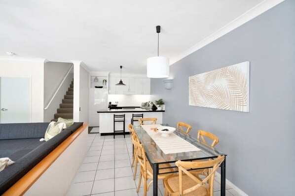 Una cocina moderna con armarios blancos, una mesa de comedor con sillas y una escalera que sube a otro nivel.