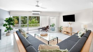 A spacious living room with a large sofa set, a glass coffee table, and a balcony with a view of greenery.