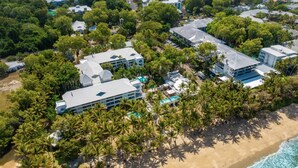 An aerial view of a resort with multiple buildings, a beach, and palm trees.