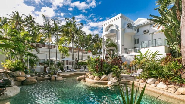 A resort with a clear pool surrounded by palm trees and lounge chairs.