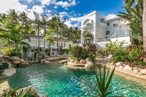 Un resort con una piscina cristalina rodeada de palmeras y sillas de descanso.