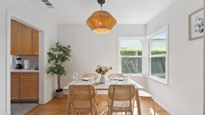 Un comedor con una mesa dispuesta para cuatro personas, rodeado de sillas de mimbre, una lámpara colgante y vistas a la vegetación a través de una ventana.