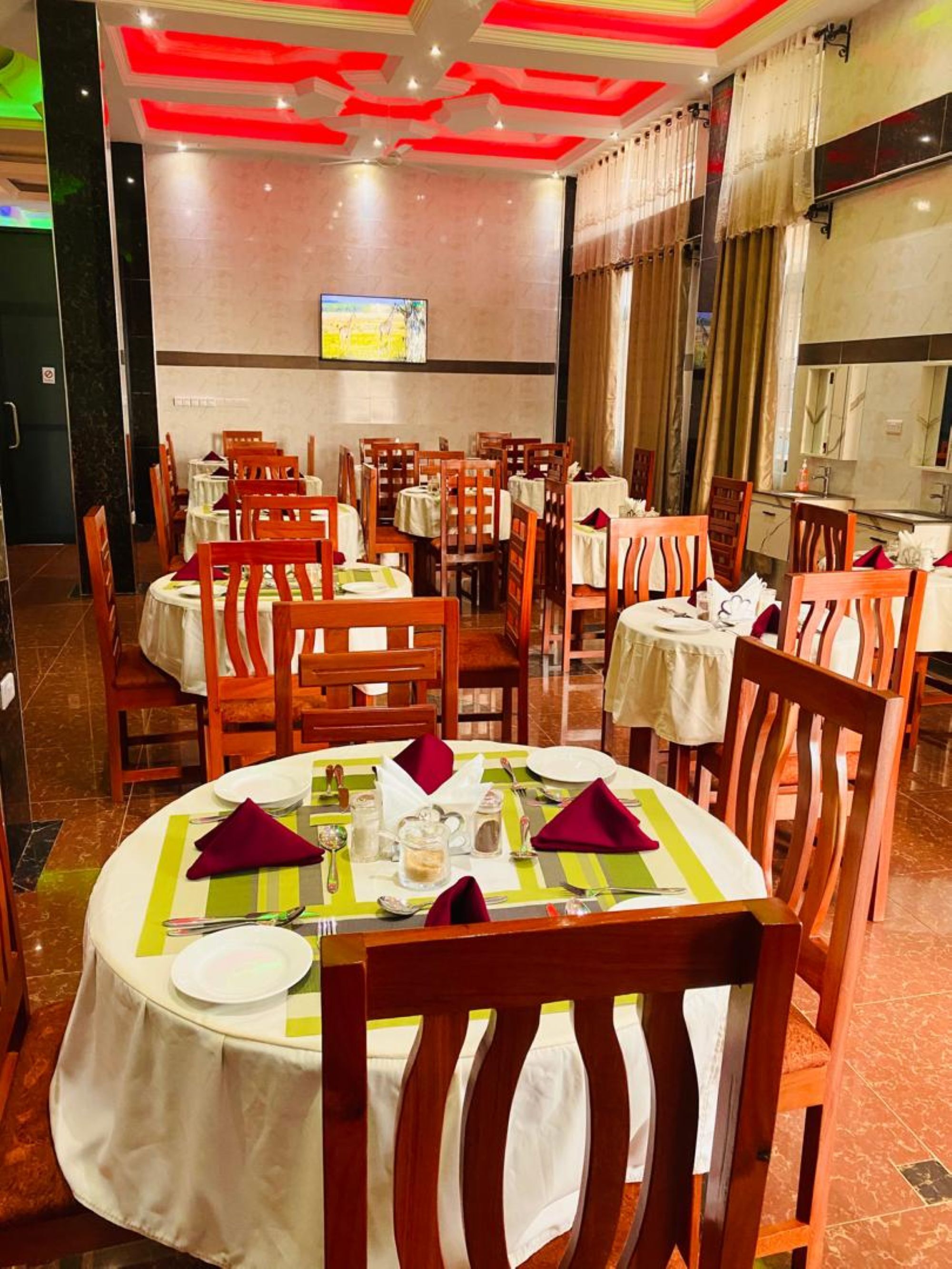A dining area with round tables, wooden chairs, and red napkins.