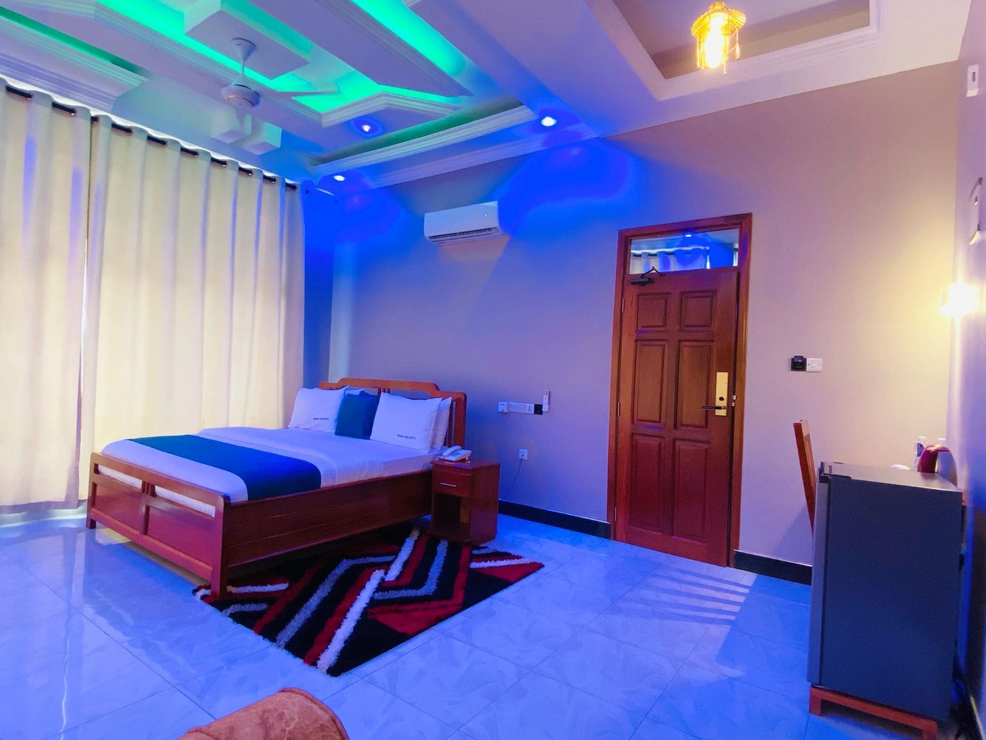 A hotel room with a bed, a desk, a chair, a wardrobe, and a ceiling fan.